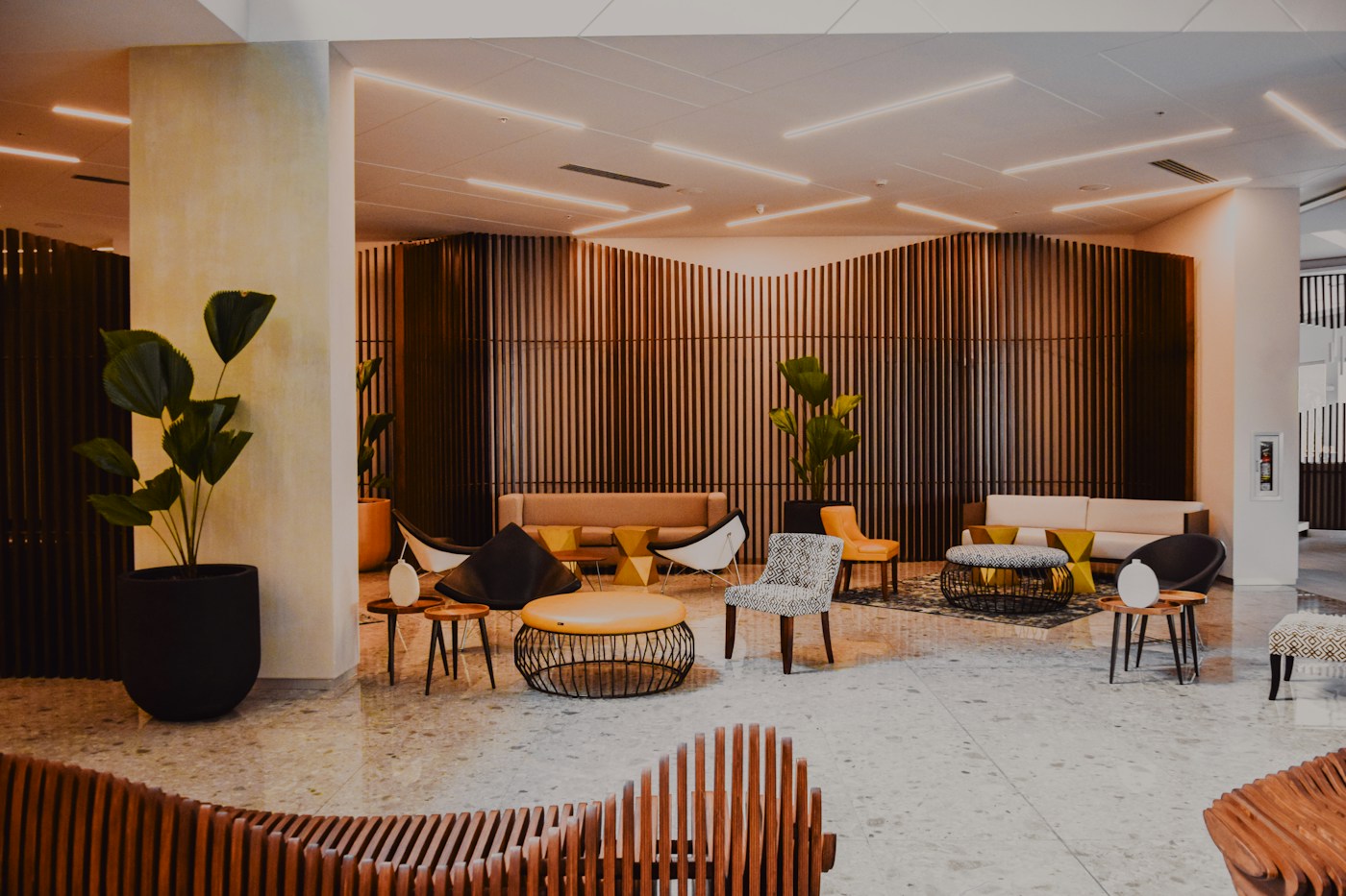 Warm modern hotel lobby with wood paneling, lounge seating, and greenery